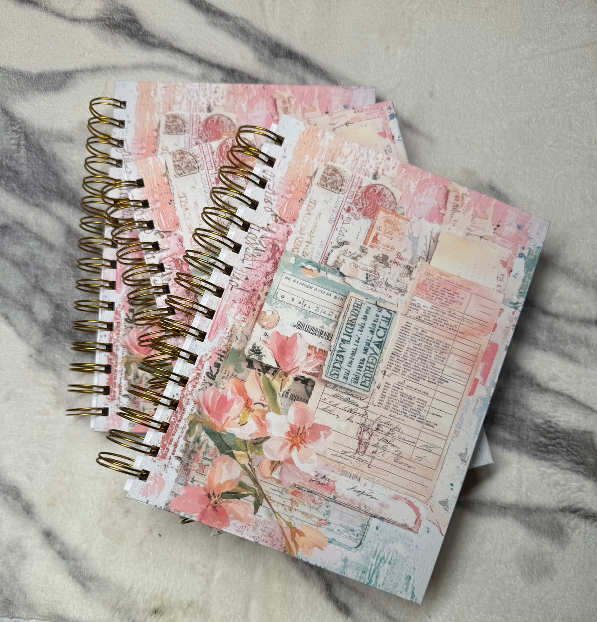 Stacked journals: Stacked pink floral collage journals with gold spiral bindings.