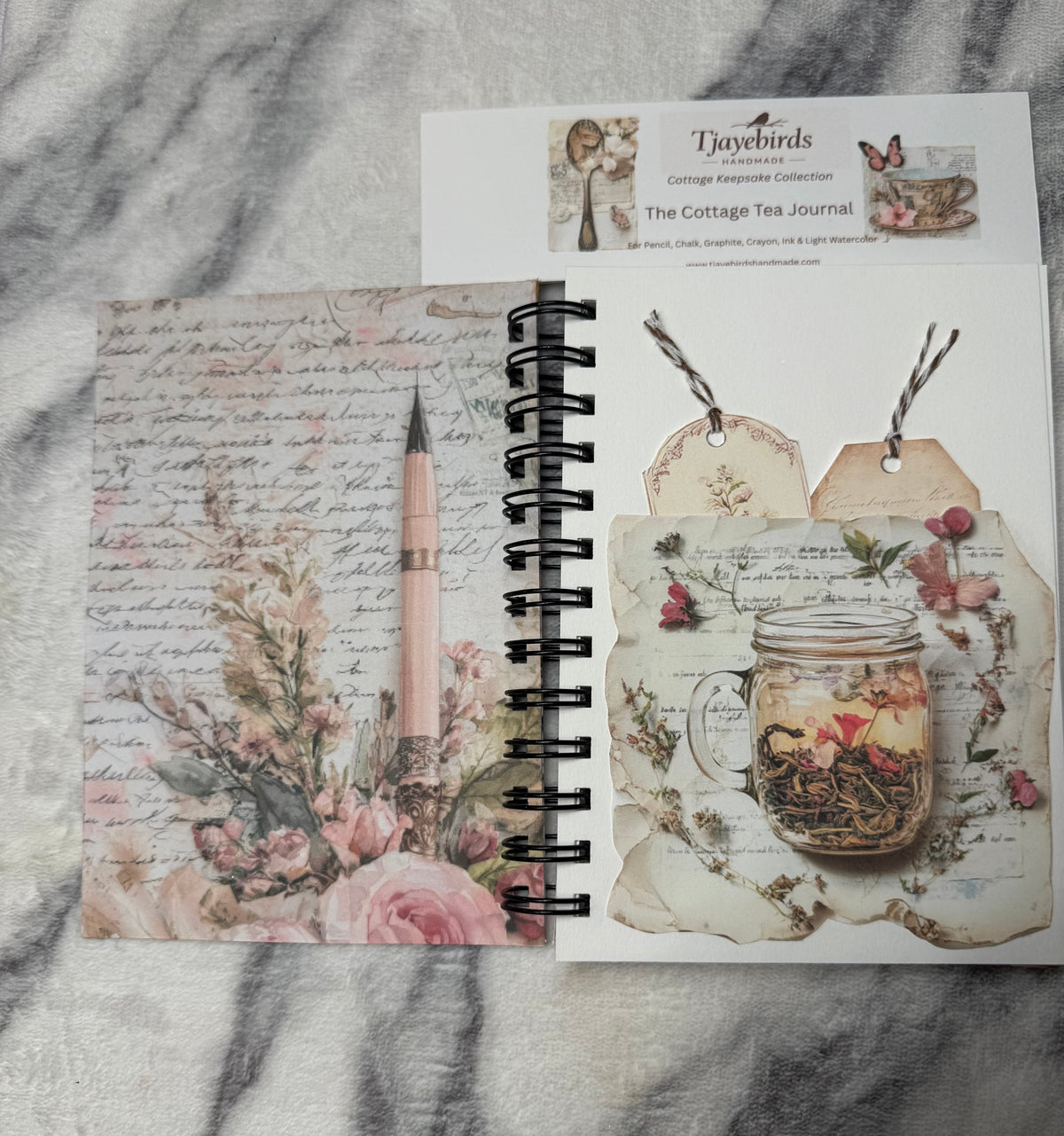 Open journal with pockets and tags: “Open Cottage Tea Time Journal showing a floral inside cover and a decorative pocket holding two tags."