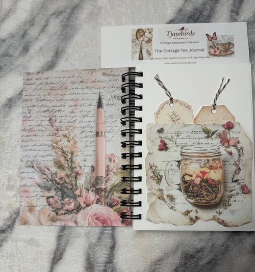 Open journal with pockets and tags: “Open Cottage Tea Time Journal showing a floral inside cover and a decorative pocket holding two tags."